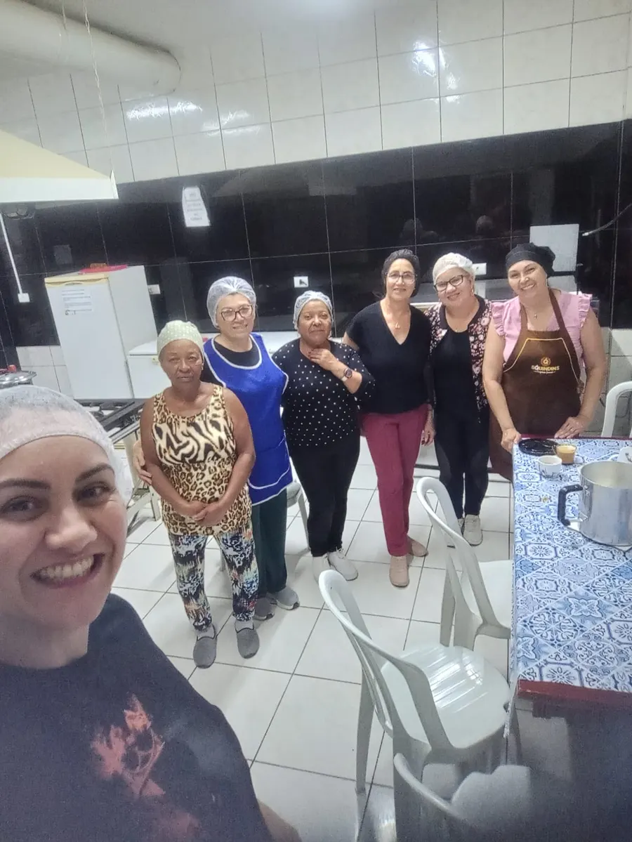 Grupo de voluntárias reunidas e sorrindo na cozinha da paróquia