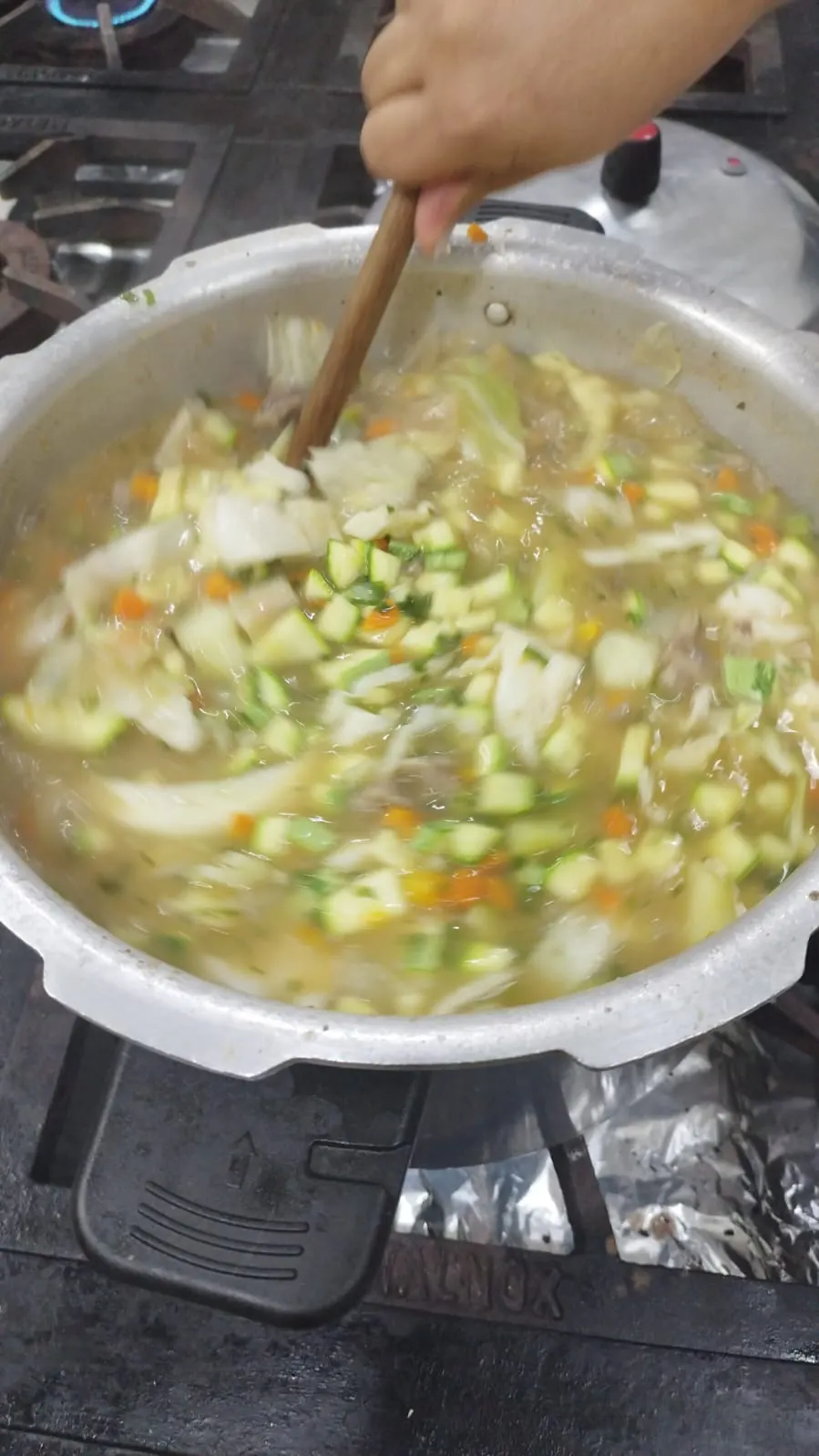 Legumes sendo refogados em uma panela grande, parte do preparo da refeição